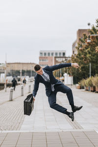 Businessman holding briefcase and jumping mid-air on footpath