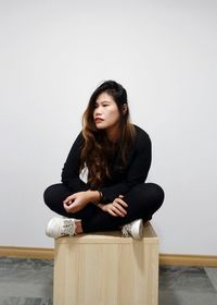 Woman looking away while sitting against wall