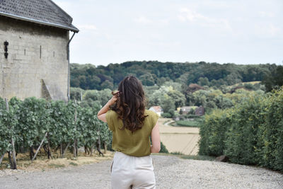 Rear view of woman standing road by farm against clear sky