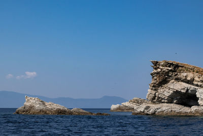 Rock formation by sea against clear blue sky