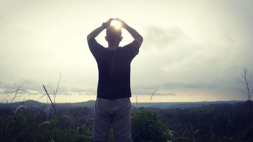 Rear view of man standing on field against sky