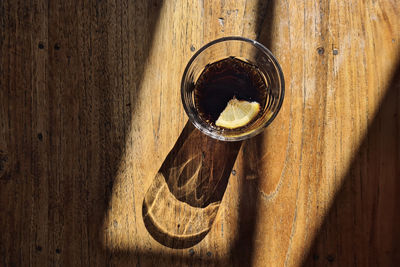 Drinking glass with cola drink. light and shadow on wooden table.