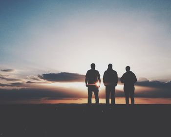 Silhouette of three people standing against sunrise