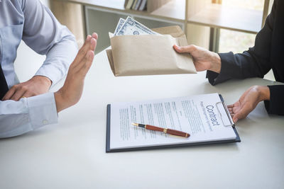 Midsection of businessman refusing bribe while colleague holding contract at desk