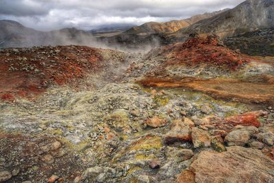 Hot springs by rock formations against cloudy sky