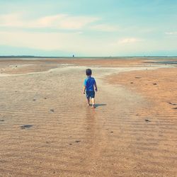 Rear view of boy on beach against sky