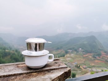 Coffee cup on table against mountain range