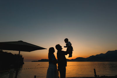 Silhouette people standing on shore against sky during sunset