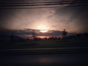 Electricity pylons on field against sunset