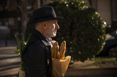 Adult man in hat holding bread and vegetable bag on street. madrid, spain