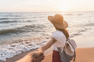 Cropped image of man holding woman hand standing at beach