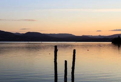 Silhouette wooden posts in lake against sky during sunset