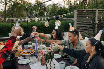 Cheerful male and female friends toasting drinks during birthday celebration in back yard