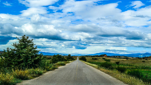 Scenic view of country road against cloudy sky