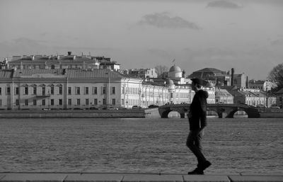 Man standing by river against buildings in city