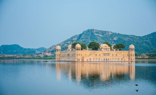 Building by lake against clear blue sky