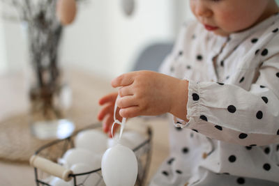 A little girl sits on a wooden table, near to her is a metal basket with easter eggs.