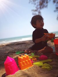 Boy playing with toys while sitting at beach against sky