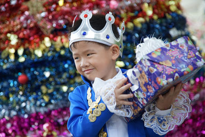 Smiling boy wearing crown holding gift box while standing in party