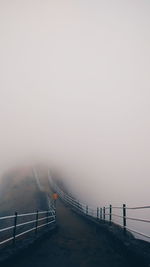 Suspension bridge in foggy weather against sky