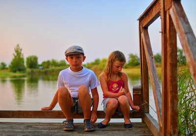 Cute children, little boy and girl are sitting on pier in the summer evening. two siblings. golden