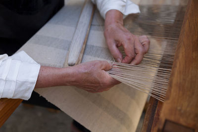 Close up on the hands of a man weaving a fabric from flax fibers with an antique hand weave machine.