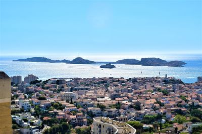 High angle view of townscape by sea against blue sky