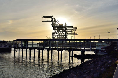 Silhouette pier over sea against sky during sunset