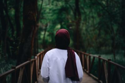 Rear view of woman standing on footbridge in forest