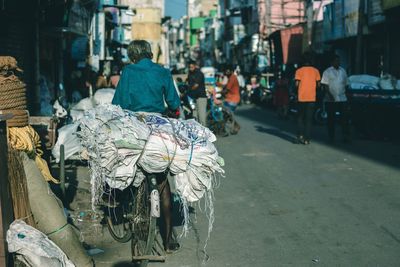 Rear view of man carrying sacks on bicycle in city