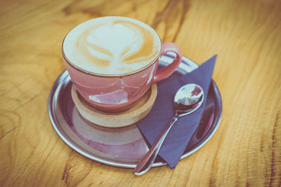 Fresh cappuccino with flower art on wooden table. ready to serve with black napkin and spoon.