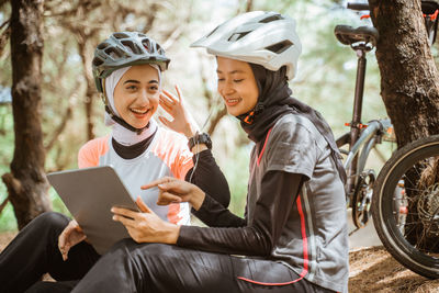 Smiling female friends using digital tablet sitting at park