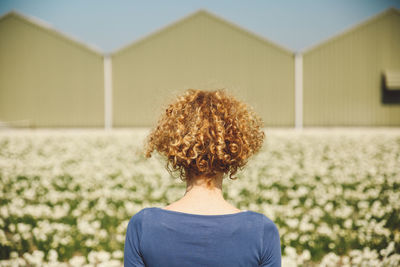 Rear view of woman with curly hair on field against barns