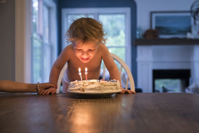 Candlelit toddler boy blowing out candles on birthday cake