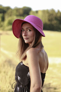 Side view portrait of woman wearing pink hat standing on field