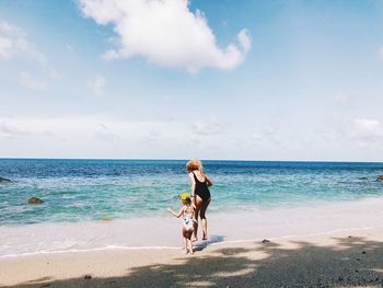 Rear view of mother and daughter at beach against sky