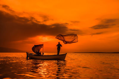 Silhouette men in boat against sky during sunset