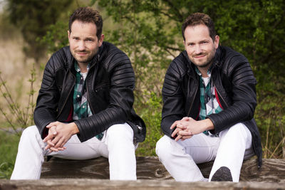 Multiple image of man smiling while sitting on wood against plants