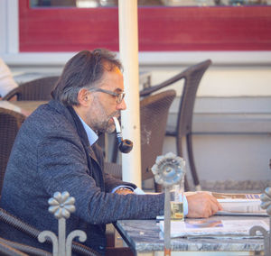 Businessman smoking pipe while reading newspaper on table