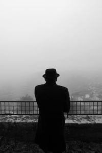 Rear view of man standing by railing against sky