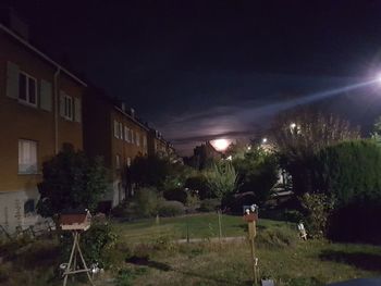 Illuminated street amidst buildings against sky at night