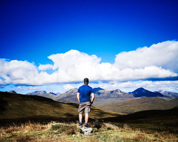 Rear view of man looking at mountains against blue sky