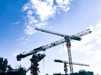 Low angle view of cranes at construction site against sky