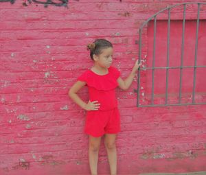 Full length of girl standing against red wall