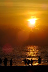 Silhouette people on beach against sky during sunset