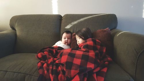 Portrait of girl with sleeping sister on sofa at home