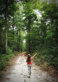 Rear view of woman with arms raised in forest