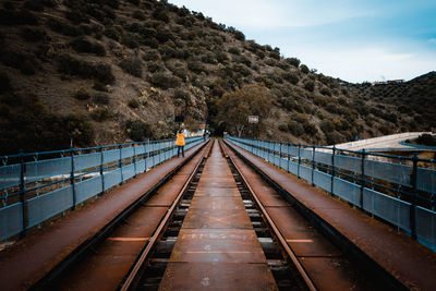 Rear view of woman standing on railway bridge against mountains and sky