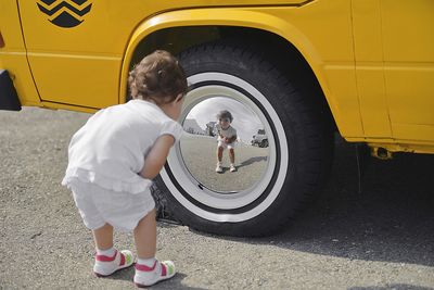 Cute baby girl looking at her reflection in car wheel