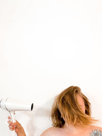 Close-up of young woman with a hair dryer against white background